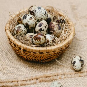 From above of heap of quail eggs on hay in wicker bowl placed on sackcloth